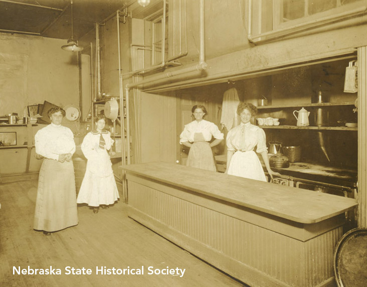 Four women stand in a kitchen setting, date and place unknown