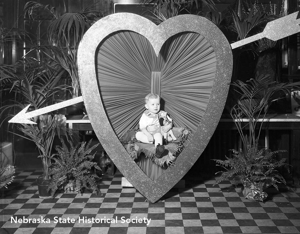 A Valentine's Day portrait of a child sitting in a large heart with an arrow through it, Omaha 1934