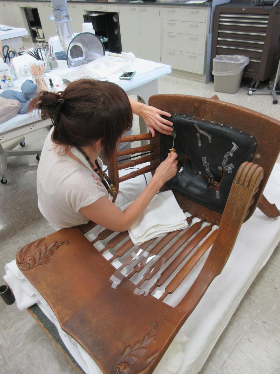 conservator applies adhesive strips to leather seat