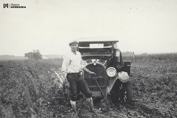 man and shovel and stuck Model-T era car on muddy rural road