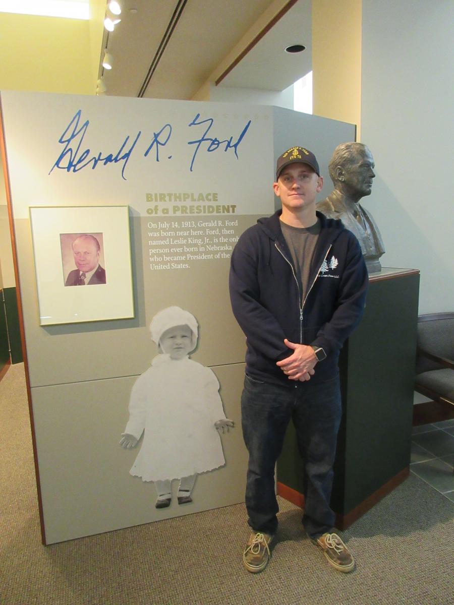 Chris Tysor stands in front of bust of Gerald Ford and photo of young Gerald Ford.