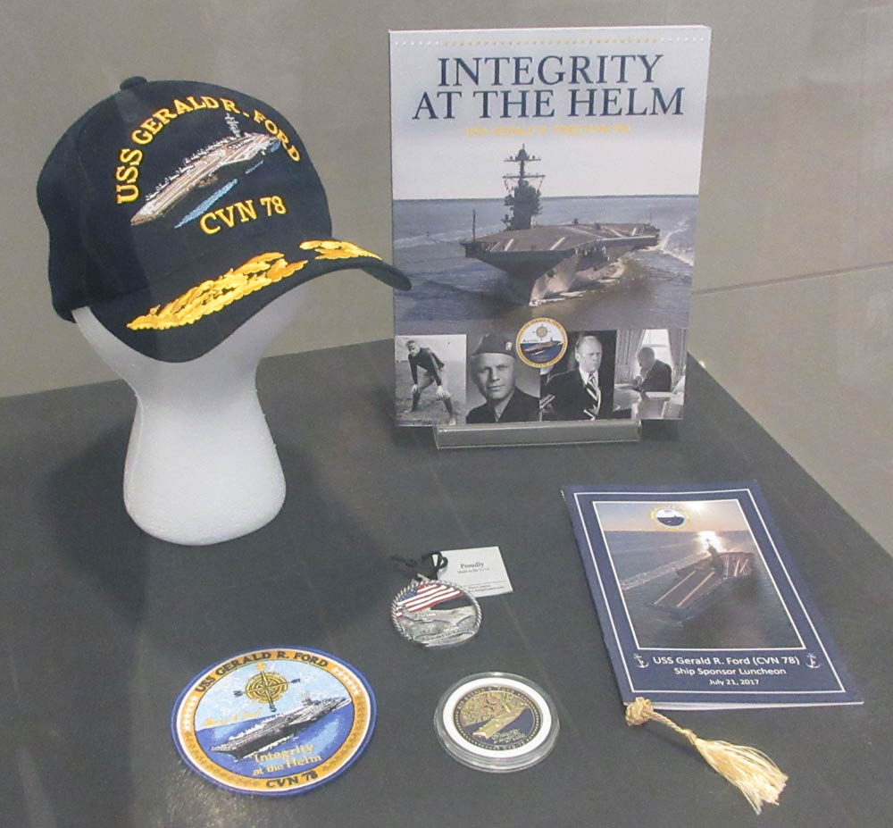 Hat, books, medal, and patch commemorating the commissioning of the USS Gerald Ford in display case.