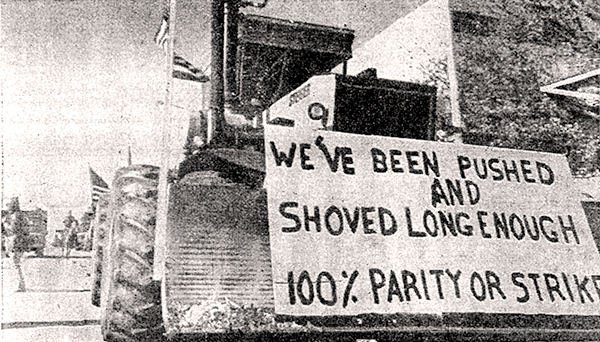 Tractor with snowplow and sign: "We've been pushed and shoved long enough. 100% parity or strike"