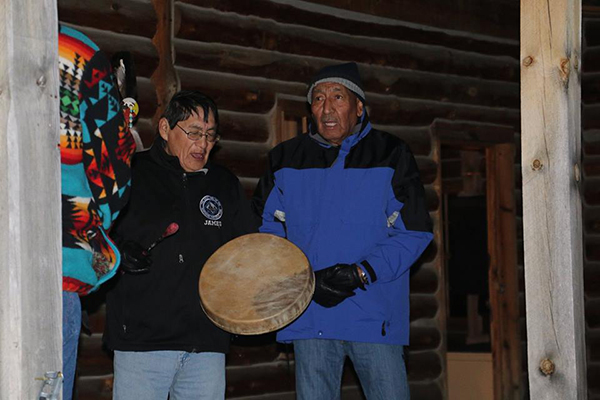 Two Northern Cheyenne men in winter clothes, holding a drum 