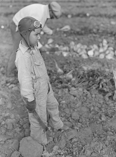 Little boy wearing aviator helmet and goggles and holding machete