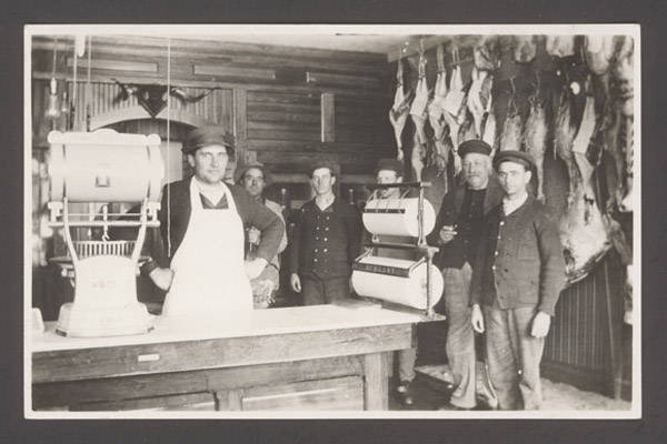A butcher and his helpers inside a butcher shop.