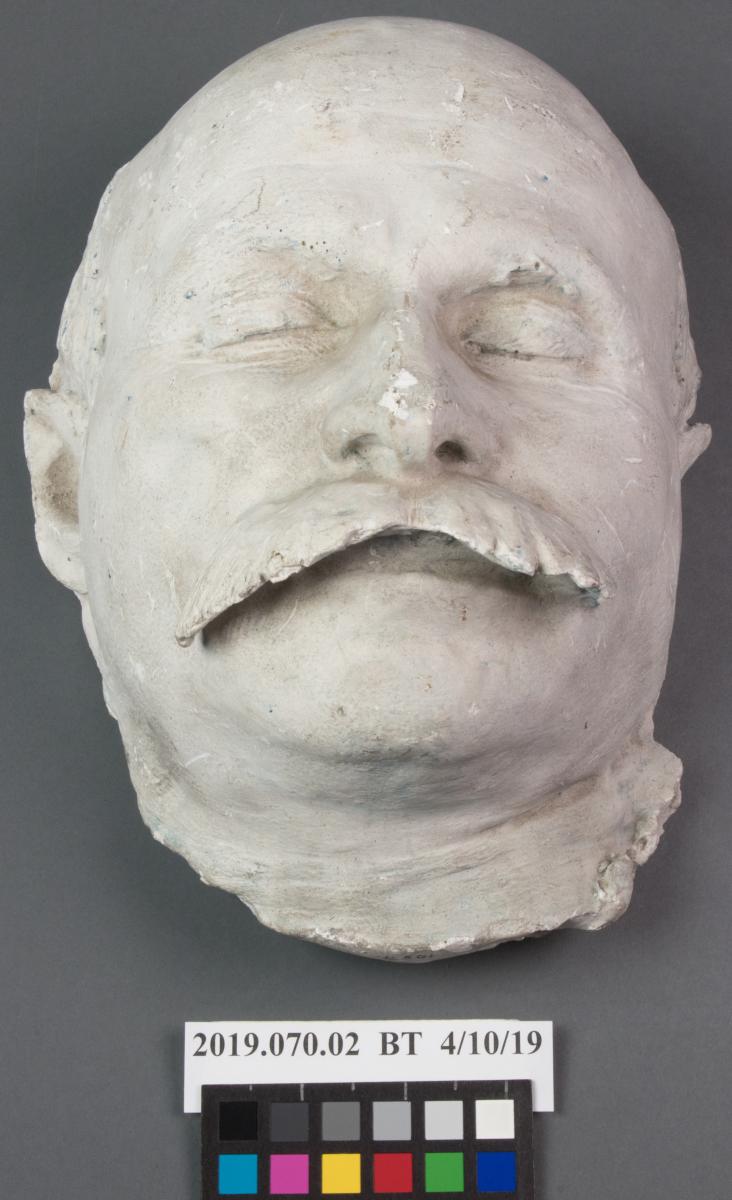 plaster death mask of a man with a large mustache, before treatment, grey in color with loss on nose
