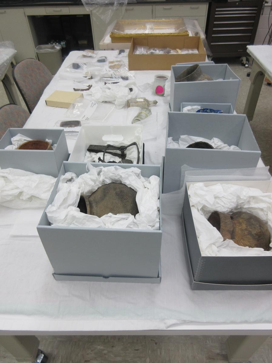 Assortment of archaeology objects, glass bottles, ceramic pots, metal tools, in boxes and bags on a table