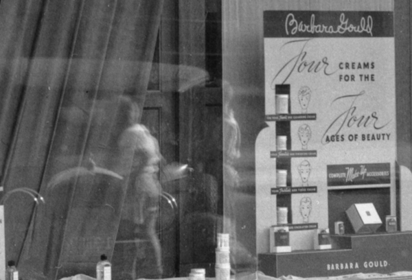 Detail of the corner drug store. A makeup ad in a window display.