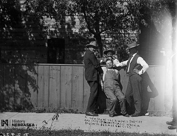 Three men restrain a fourth man. Caption scratched onto photo reads: "A new fad of the Kearney sheriff and chief of police Trindle when a bad man strikes the city."