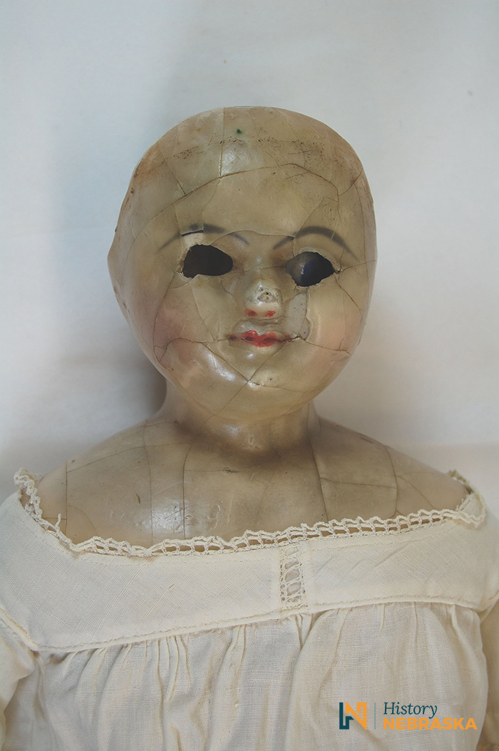 Close up image of a bald doll with a white outfit, makeup, and an eye missing.