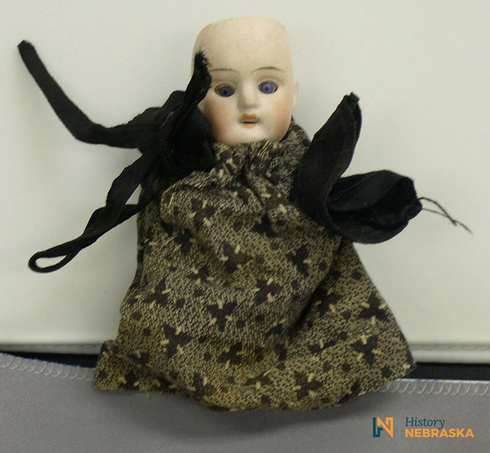 A bald doll with a brown dress and ribbon ties.