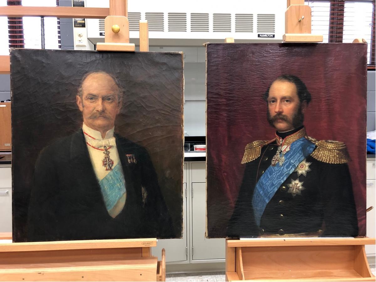 two painted portraits of men with facial hair, medals, blue sashes. Canvases on easels, before treatment