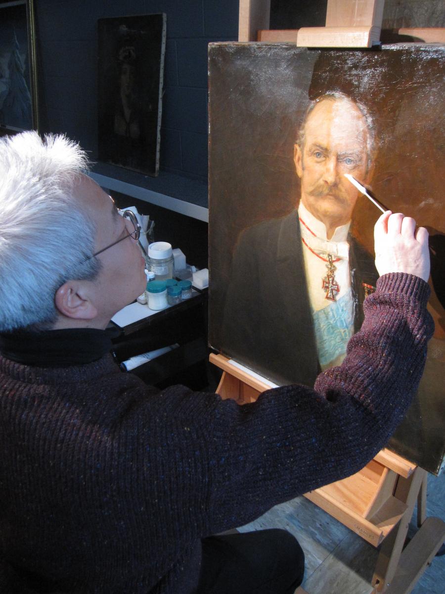 man removes varnish with cotton swab from section of portrait of man
