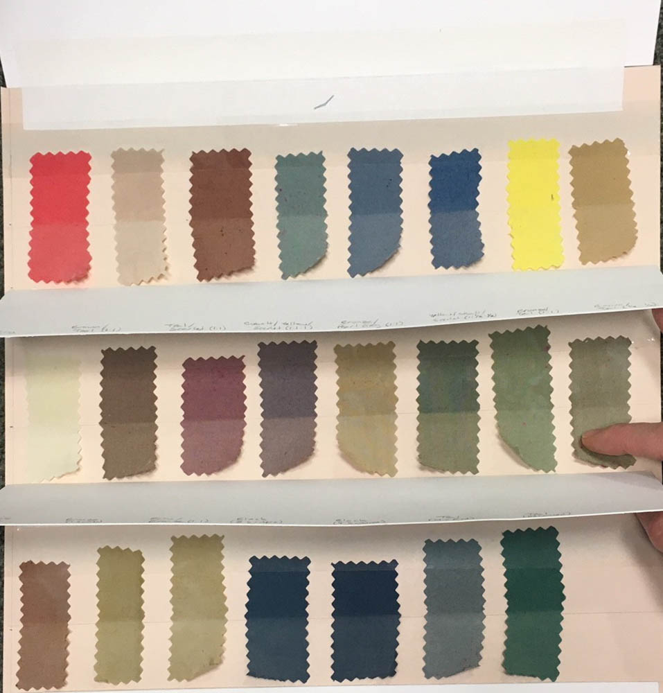Detail photograph of a board with dyed cotton fabric swatches. The blotter covering the top half of the rows of swatches is lifted to reveal the original dye colors underneath. The exposed bottom half are noticeably faded.