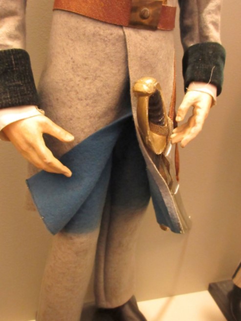 detail photo of the waist of a doll in military uniform. The hem of the grey coat is pulled aside to show the original blue color underneath.