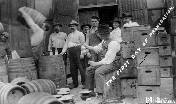 Postcard of men standing around barrels and crates, lableled "THE FIRST DAY OF PROHIBITION."