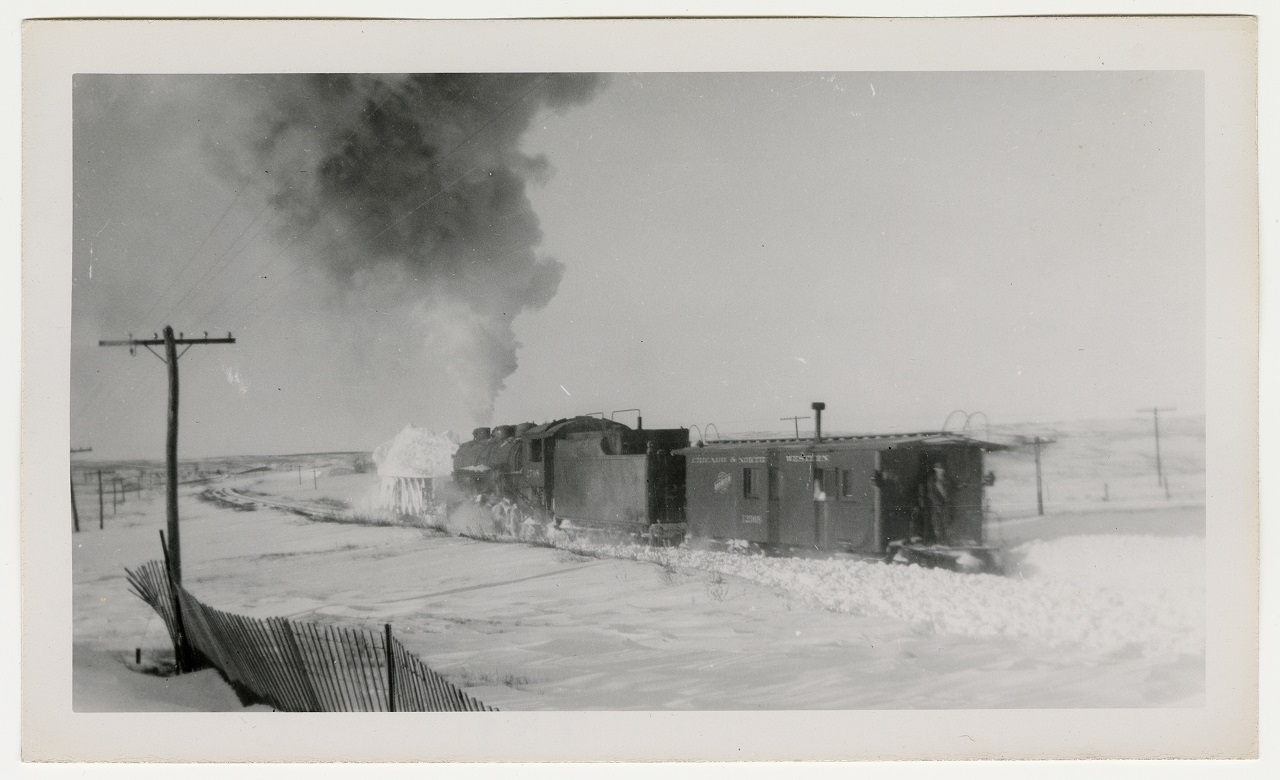 Photo of a railroad locomotive and caboose pushing a snow plow through snow.