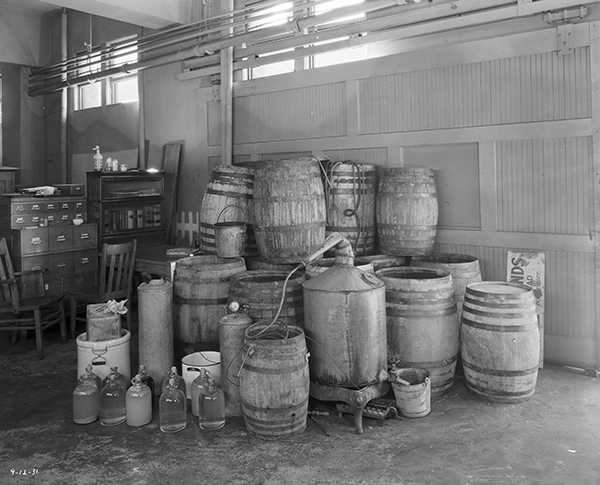 Still, barrels, and jugs of moonshine stacked inside a building