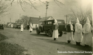 Several hooded Ku Klux Klan members follow a hearse in a funeral procession in Chadron, NE, in 1926. RG5832-1