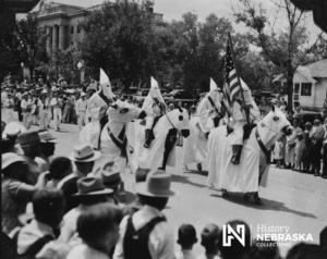 Ku Klux Klan members carry an American flag in a parade in Gering, NE, ca.1920s. RG4909-1-29