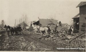 A picture postcard of a horse-drawn buggy & a horse-drawn wagon amid the ruins of houses in Omaha, NE after the 1913 tornado.