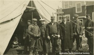 A picture postcard of a crew of men in front of a tent by a house getting new rafters in Omaha, NE after the 1913 tornado.