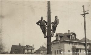 A picture postcard of two men on a pole, presumably fixing downed power lines in Omaha, NE after the 1913 tornado.