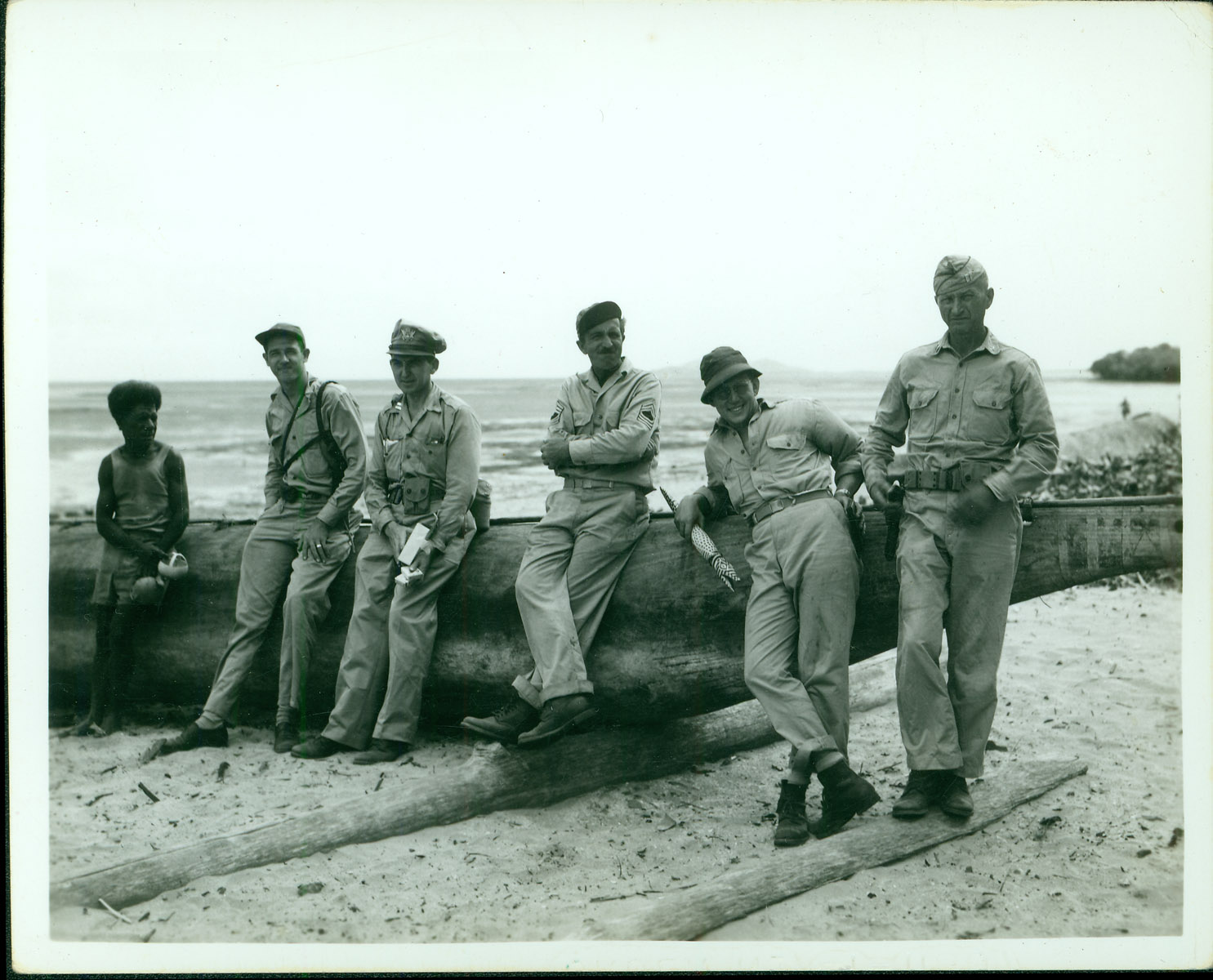 Robert Merchant, four 90th Bomb Group personnel and one native man lean against a native boat while stationed in New Guinea. Third from the left is Captain Norman J. Lawler.