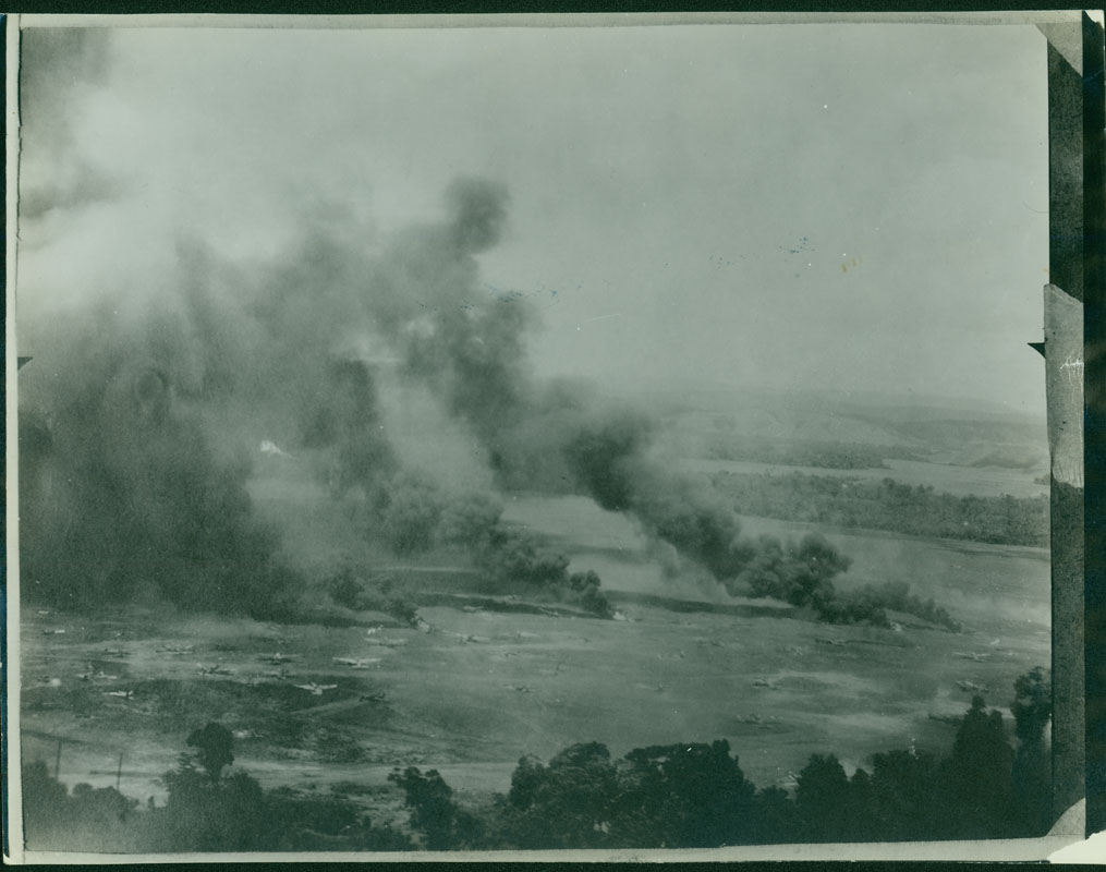 An aerial side view of crashed Japanese planes with smoke rising from them. The back of the photo reads, "Hollandia Air Drome". There were three major airdromes in the Hollandia area. The Allies captured all three, with little opposition from the Japanese.