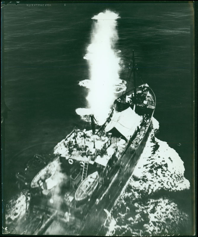 This shows an aerial view of bombs exploding over land and water. The back of the photo reads "Salamaua Peninsula" Salamau was originally intended by the The Japanese originally intended Salamaua as a staging post for an assault on Port Moresby, because taking control of the Australian territory of New Guinea was a major aspect of Operations Mo, Japan’s overarching plan to isolate Australia and New Zealand from the United states. However, the plan to take Port Moresby was abandoned after several failed attacks. Instead, the Japanese converted the Salamaua port into a major supply base.