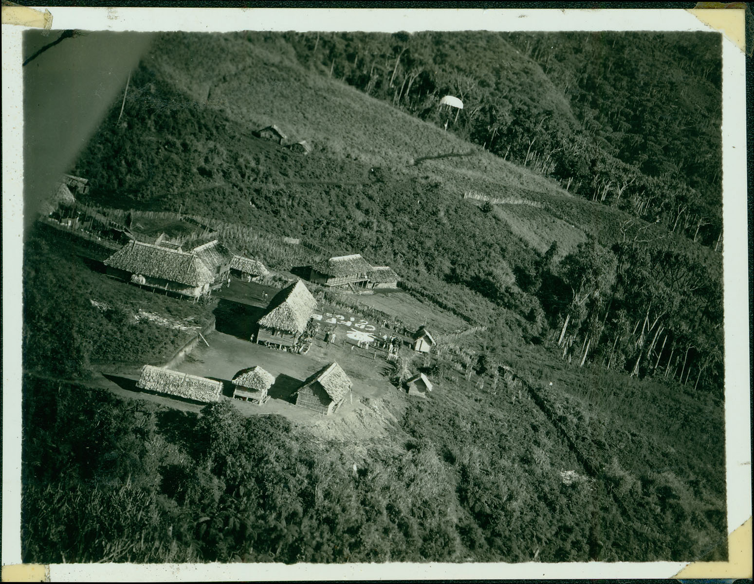 An aerial shot of the New Guinea native village that took in the ten Army officers. The parachute floating down contained either a letter or supplies for the officers.