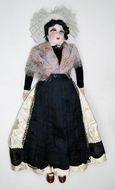 Doll (NSHS 7144-123) Doll wearing a regional costume with brown leather shoes, a heart-shaped white mother-of-pearl locket and white earrings. There is a note that says: "From people of Boulogne." 