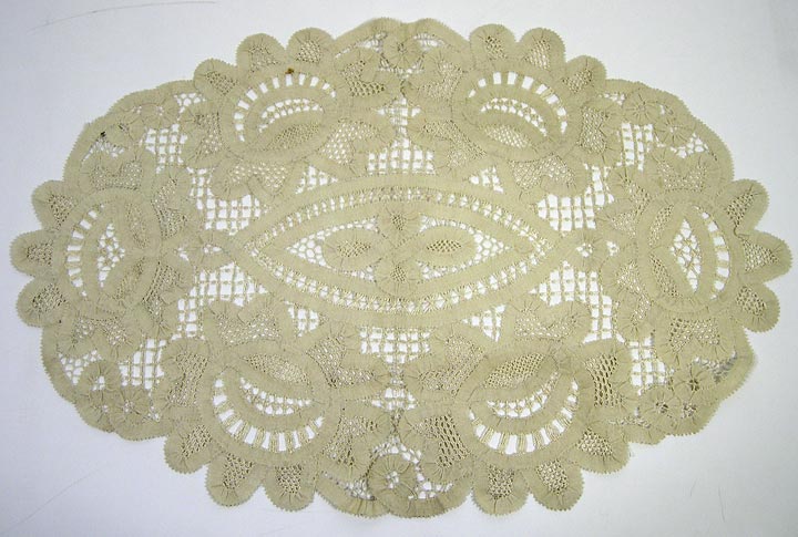Doily (NSHS 7144-207) Macramé doily with floral patterns surrounding the oval center.