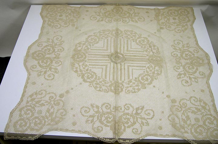 Table throw (NSHS 7144-208) Macramé table cover that has floral patterns inset and a geometrical pattern in the center area. 