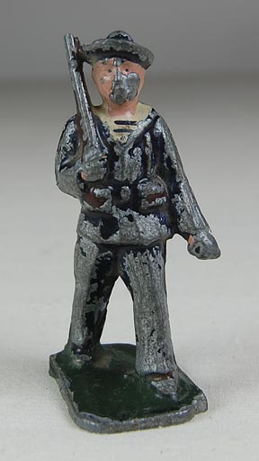 Toy Soldier (NSHS 7144-39) Miniature toy soldier marching with a rifle. The silver paint is worn off and he has a painted pink face and a green base. 