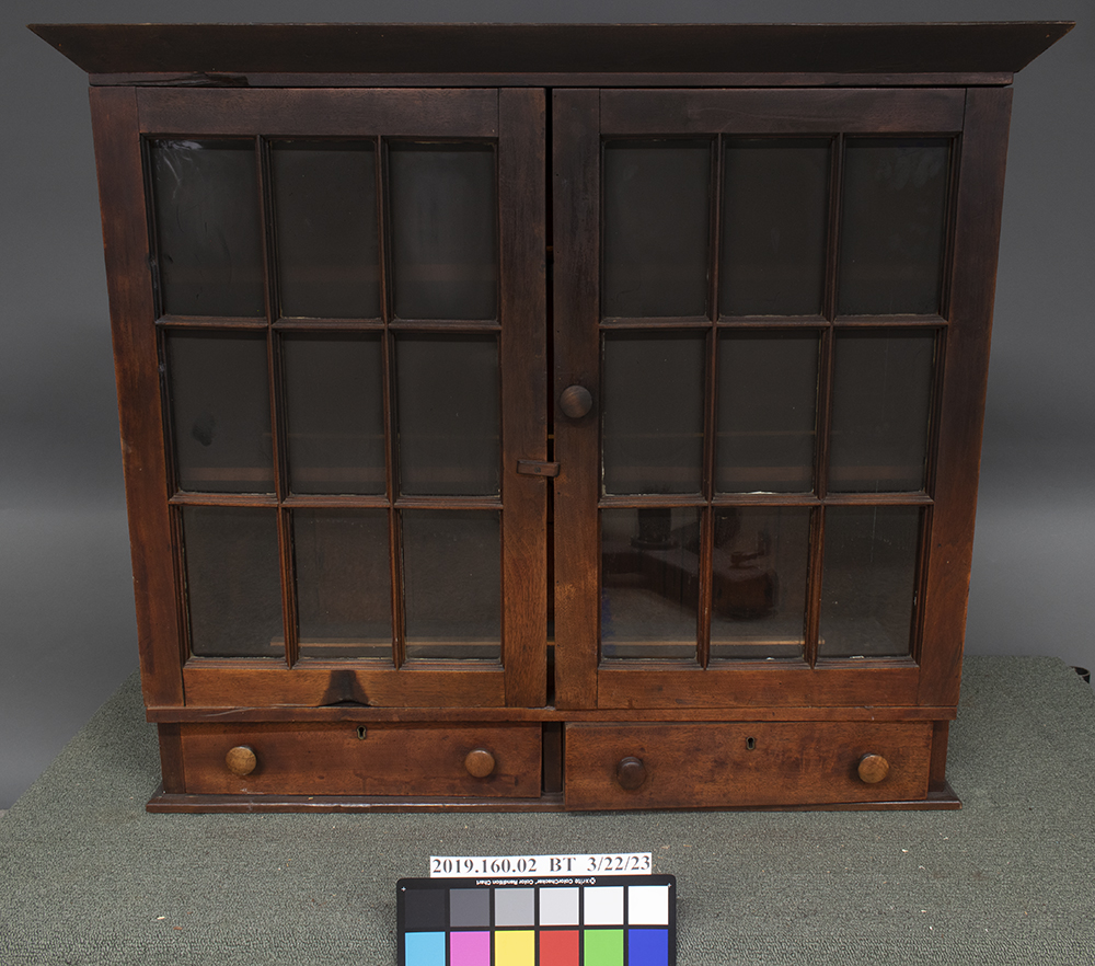 The top of a wood sideboard with glass windows before treatment. The soot layer is darker toward the top of the cabinet, and the glass panes are almost completely obscured.