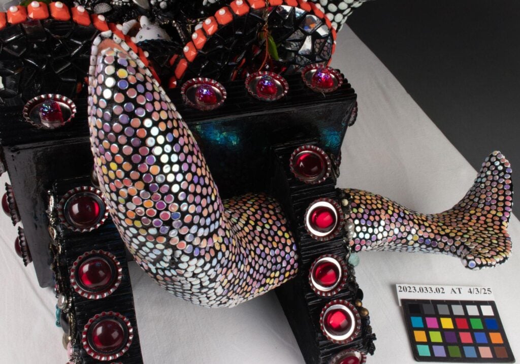 Sculpture with a multicolored, scale-patterned mermaid tail attached to a black base decorated with red and white gems; color calibration card included.