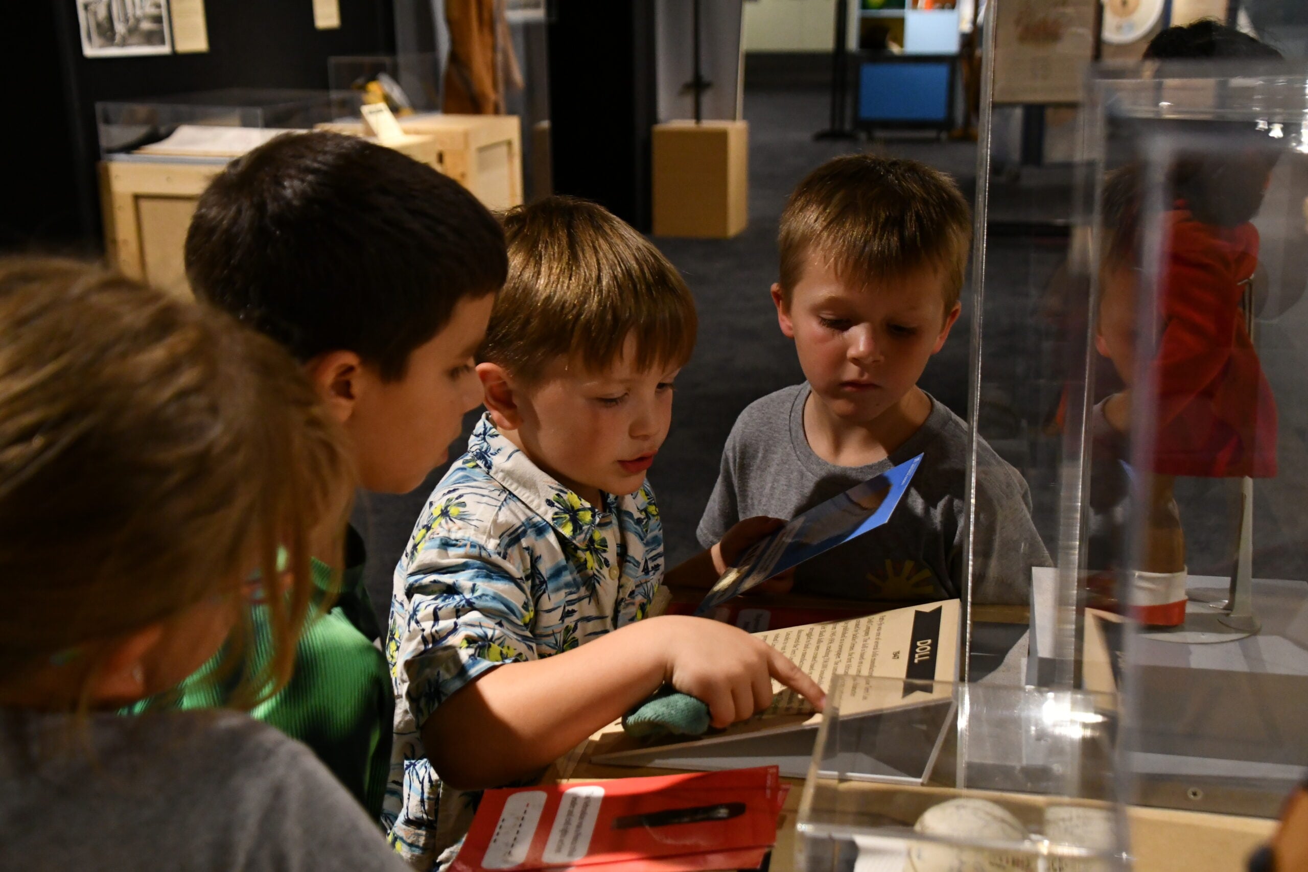 Four young children closely examine and read a display case with artifacts and information at a museum exhibit during one of the Summer Workshops.
