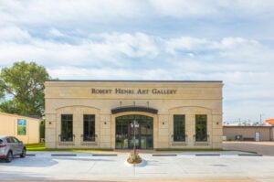 A beige stone building labeled "Robert Henri Art Gallery" with large windows, a central arched entrance, and a small landscaped area in front.