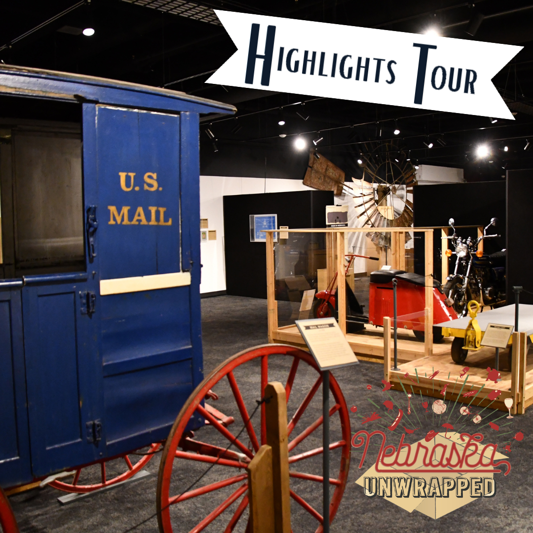 Hands-On History NE Unwrapped Exhibit of historical items including a blue U.S. Mail wagon, windmill, and other artifacts, with signs reading "Highlights Tour" and "Nebraska Unwrapped.