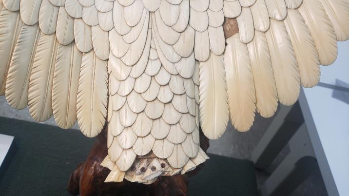 Close-up of an intricately carved ivory sculpture resembling the underside of a bird's wing, displayed on a green surface.