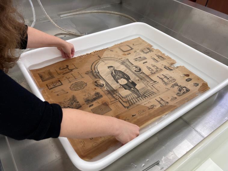An image of a conservator washing the print in a white rectangular plastic tub filled with pH-controlled water.