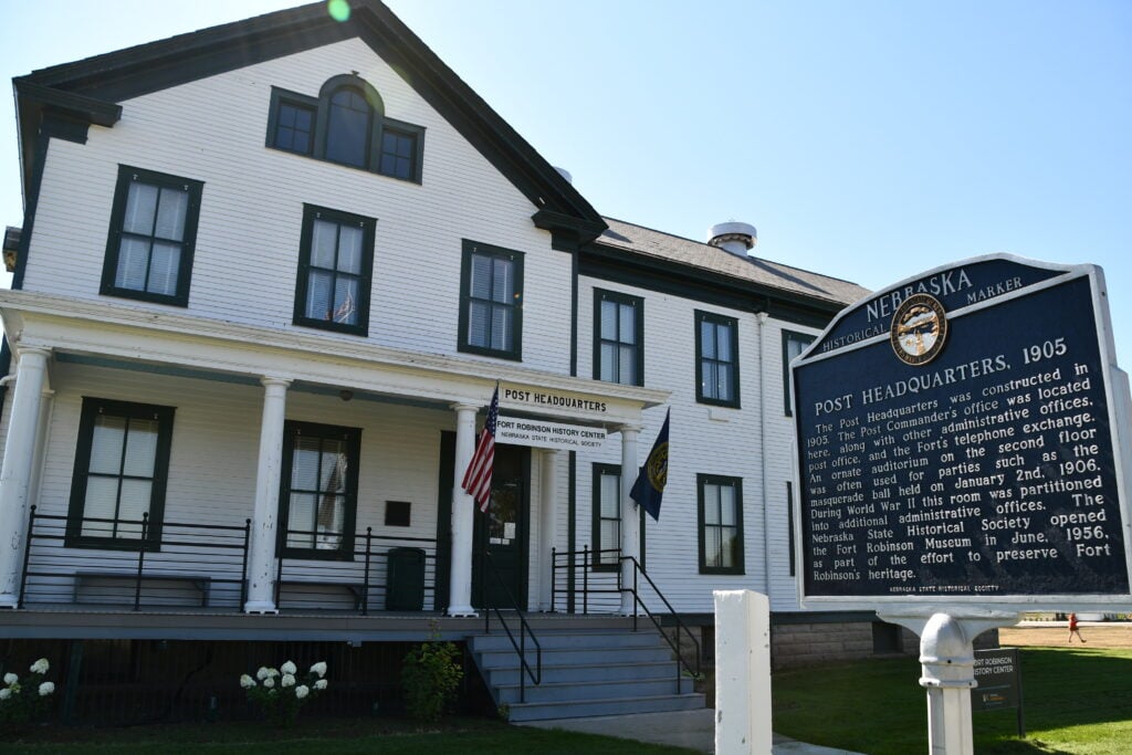 A historic white two-story building labeled "Post Headquarters" stands behind a Nebraska State Historical Marker describing its 1905 origins.