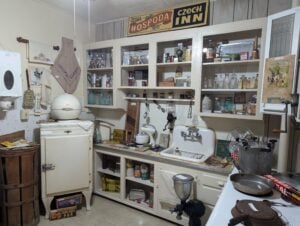 Vintage kitchen with white cabinets, old appliances, canned goods, utensils, and Czech decor signs displayed above the shelves.