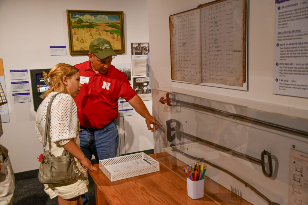 A father and daughter observe a museum display of branding irons and historic documents; the man is explaining something and pointing at the exhibit.