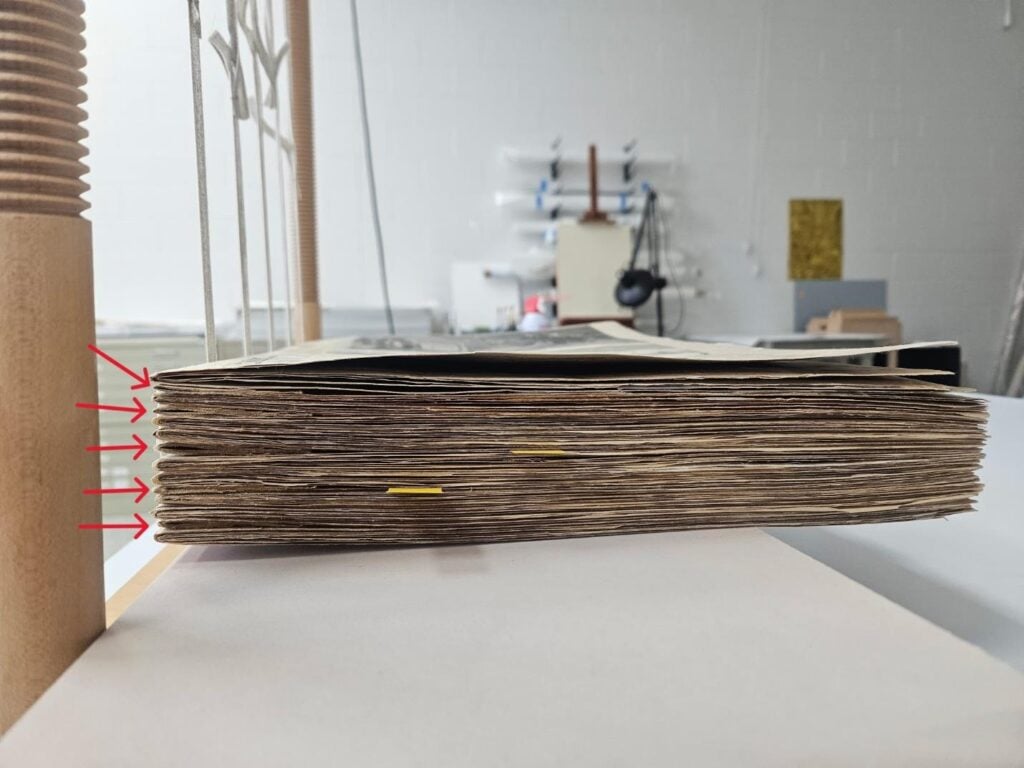 A stack of aged, slightly warped papers with yellow tabs is shown from the side; red arrows indicate a section near the left end.