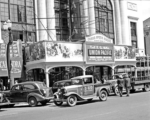Black-and-white photo of vintage cars parked in front of the Omaha Opera House, advertising "Union Pacific." Several people are gathered on the sidewalk.