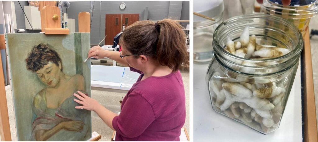 A person restores a painting of a woman on an easel; next to it is a jar filled with silkworm cocoons.