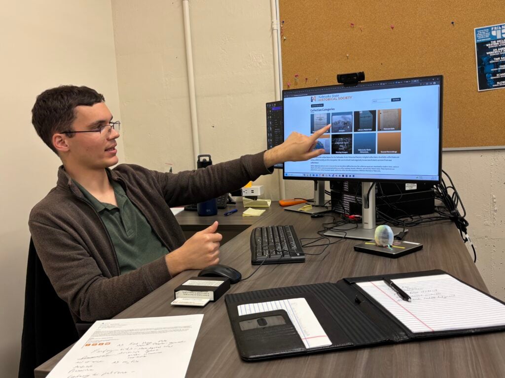 A man points at a Nebraska State Historical Society website displayed on a computer monitor.